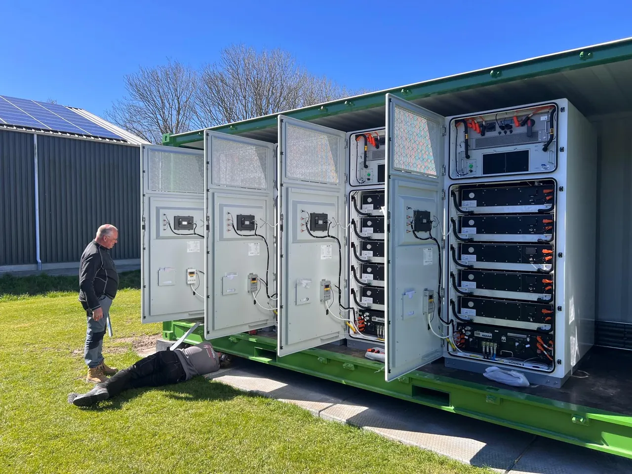 Batterijcontainer met vier geopende kastdeuren en een monteur ernaast